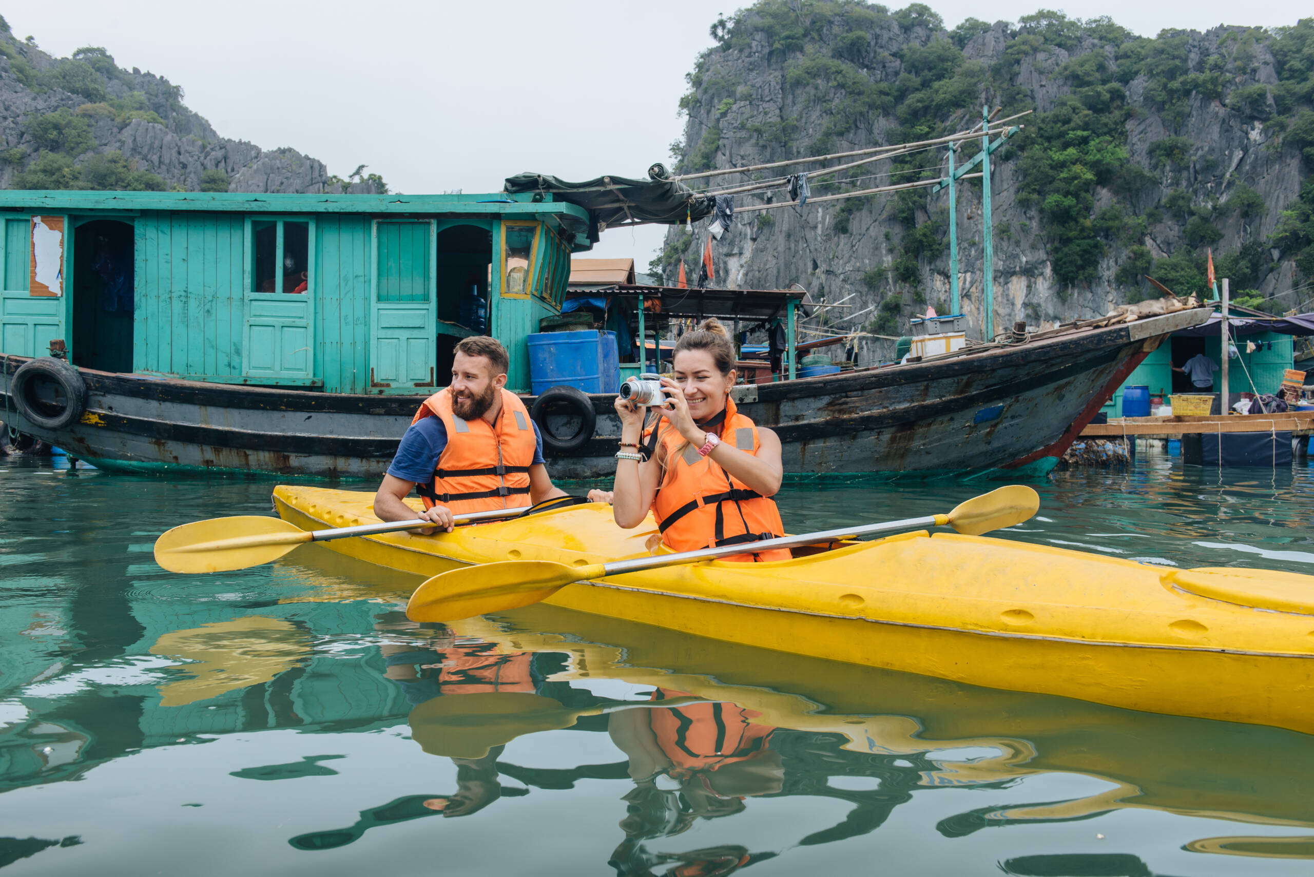 viaggio in vietnam 15 giorni - Una coppia esplora un villaggio galleggiante in kayak e scatta fotografie dalla barca. Baia di Halong